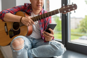 leisure, music and people concept - close up of man with guitar and smartphone sitting on windowsill