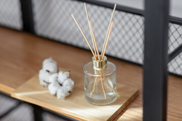 Fototapeta na wymiar aromatherapy and decoration concept - close up of aroma reed diffuser and cotton flowers on shelf at home