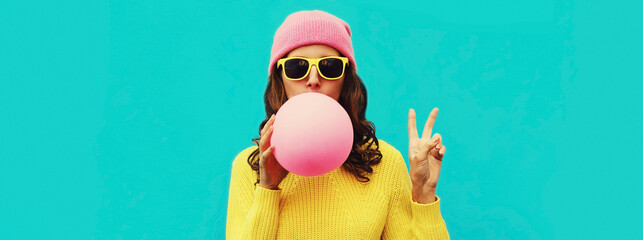 Fashionable portrait of stylish cool young woman inflating chewing gum wearing an yellow knitted...