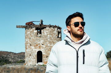 Handsome man with sun glasses on vacation. He is standing on old windmill. 
