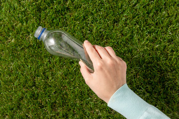 environment, volunteering and ecology concept - close up of hand removing empty used plastic bottle...