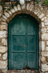 Fototapeta na wymiar A wooden old green door of stone house. Very symmetrical photo. Vintage architectural elements.