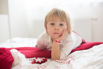 Naklejka premium Cute child, blond boy, playing with white and red bracelet