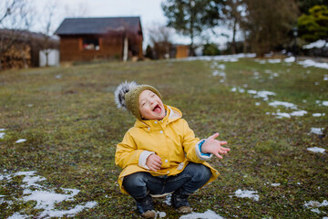 Happy little boy with Down syndrome outside in garden in wnter having fun.