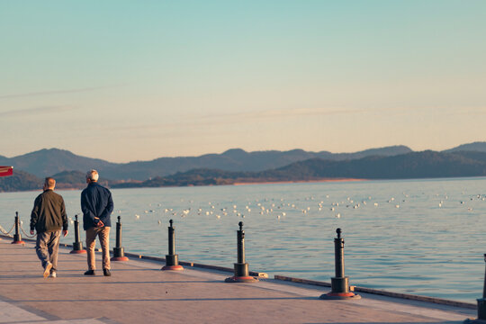 Two elderly man walking by lake at sunset. Retirement and friendship concept. 