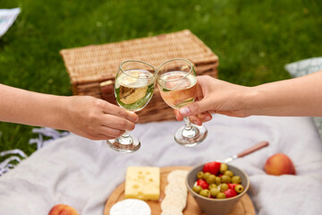 Obraz na płótnie Canvas leisure, food and drinks concept - close up of hands hands clinking wine glasses above picnic blanket at summer park