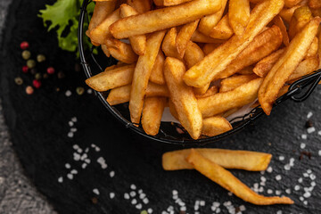 Fresh hot french fries with salt and spices on cutting board on wooden table background, unhealthy calories meal