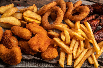 take away fast food products fried chicken with french fries and nuggets meal, junk food and unhealthy food on a wooden board. banner, menu, recipe place for text