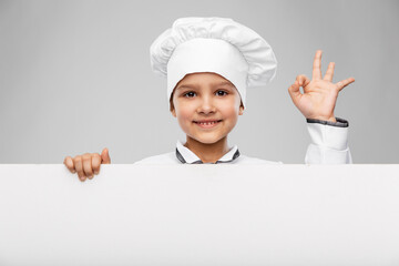 cooking, culinary and profession concept - happy smiling little girl in chef's toque and jacket with white board showing ok gesture over grey background