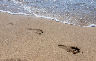Footprints of a man on the yellow beach sand from walking barefoot by the sea with water that washes away the footprints.
