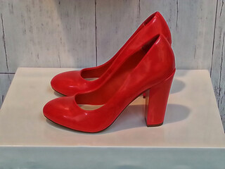 displayed on a neutral coloured geometric box shape a pair of shiny red leather ladies shoes