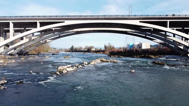 drone shot flying over river and under a bridge.