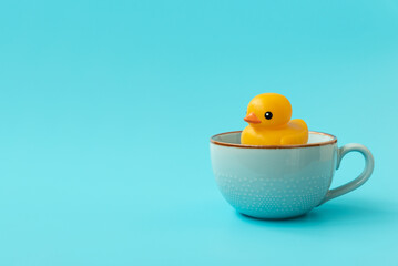 Yellow rubber duck swimming into cup of tea on blue background. Creative summer vacation concept