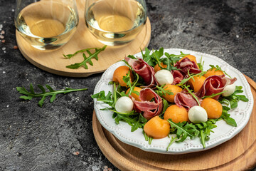 Cantaloupe melon with prosciutto or jamon, mozzarella and green basil leaves, traditional Spanish and Italian appetizer served with wholemeal grissini, top view