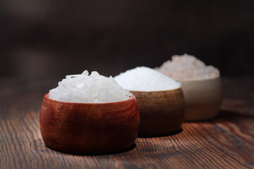 Different natural types of salt on a wooden background. Salt crystals in a wooden container