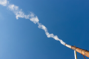 a plume of smoke or steam from an industrial smokestack on a clear blue sky