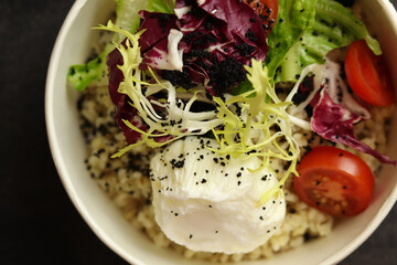 Healthy bowl with poached egg, bulgur, tomatoes and lettuce. on a dark background in an eco paper box. Healthy food delivery concept.