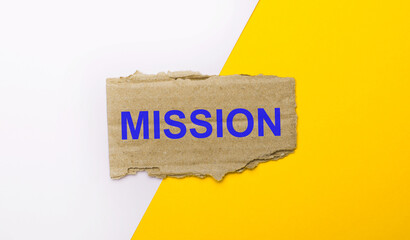 On a white and yellow background, brown torn cardboard with the text MISSION