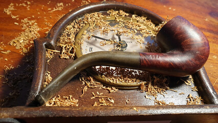 wooden smoking pipe on top of an old clock among loose tobacco, announcing world day of smoking...