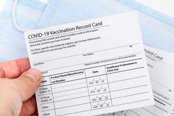 Fototapeta na wymiar Womans hand holds coronavirus vaccination record card on background blue medical mask. Concept of defeating Covid-19 - Image