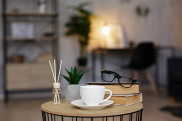 reed diffuser, cup of tea or coffee and books on table in living room