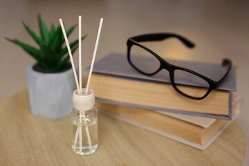 close up of reed diffuser, books, glasses and house plant on the table