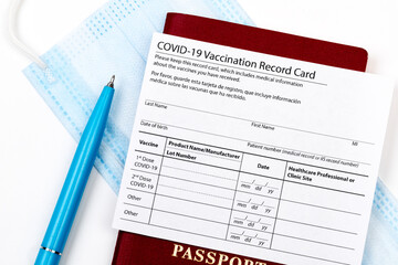 Obraz premium Coronavirus vaccination record card, biometric passport and blue medical mask on light gray desk. Concept of defeating Covid-19. Vaccination as prerequisite for travel - Image