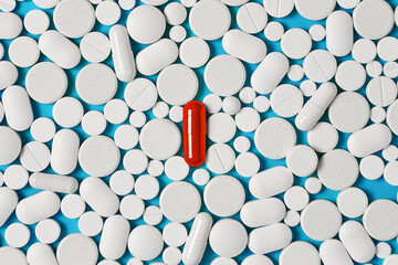 the concept of unusualness and eccentricity. Bright red pill on a background of a large number of colorless pills - obrazy, fototapety, plakaty