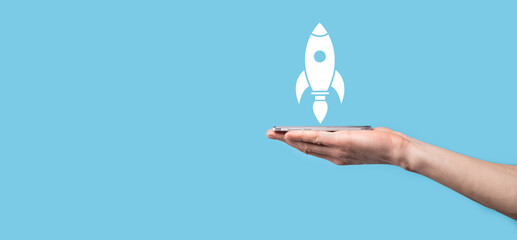 Male hand holding rocket icon that takes off, launch on blue background. rocket is launching and...
