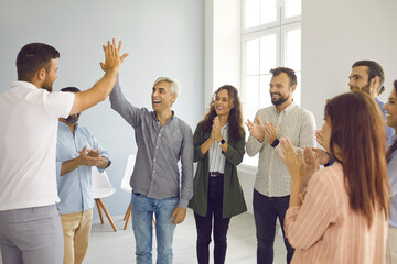 Cheerful and successful male colleagues give each other five for good job during business meeting. Happy business team standing in circle in office rejoices and applauds their successful colleagues.