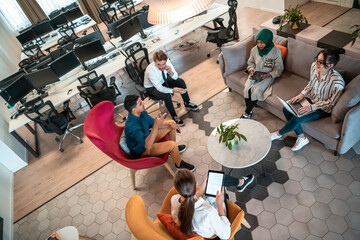 Top view photo of Multiethnic startup business team having brainstorming in relaxation area of modern office interior working on laptop and tablet computer