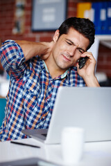 Work is getting to him. A stressed young entrepreneur rubbing his neck while on the phone to a client.