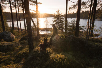 Woman and dog enjoying sunrise in the forest by a lake