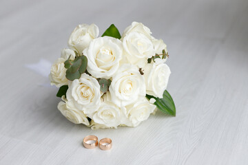 Marriage day setting with bridal bouquet of pink roses, white brides shoes and wedding rings sitting on wooden surface, viewed in close-up