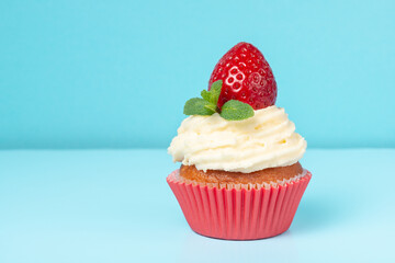 cupcake with whipped cream decorated strawberry and mint on blue background, minimalism concept