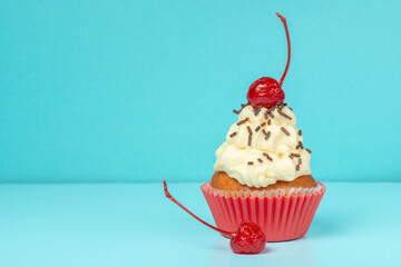 cupcake with whipped cream decorated chocolate sprinkles and maraschino cherry on blue background