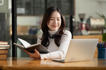 Beautiful Asian woman holding a book and looking at the laptop, she is studying online. The concept...