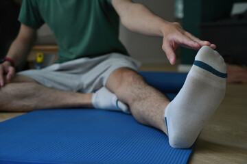 A cropped view portrait of a young man stretching his leg and touched his toes on a mat in a living room, for home exercise, yoga and a class concept.