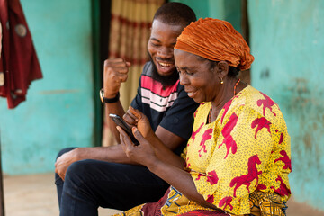 young african man and elderly woman looking at a phone rejoices