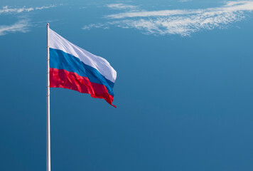 Waving Russian flag against a blue sky with clouds and empty space for text. National flag of the Russian Federation.