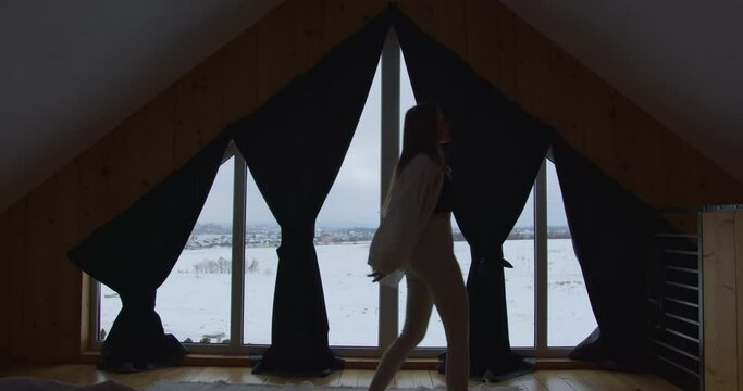 a thin fair-haired girl dances at home in front of the dormer windows. circling in a top and a light shirt. The shirt is falling apart. outside the window is winter and snow. backlit frame