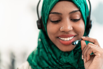 Afro Muslim female with green hijab scarf customer representative business woman with phone headset helping and supporting online with customer in modern call centre