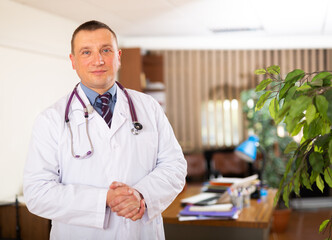 Fototapeta na wymiar Positive doctor standing in office with clipboard, holding medical history sheet
