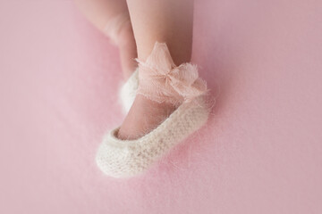 Fototapeta na wymiar Legs of newborn girl in knitted booties ballet flats with silk bows are isolated on pink background. Copy space. Soft focus.
