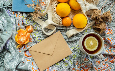 summer picnic flatlay, fruits, oranges in string bag, letter envelope, book and cup of tea on cotton blanket, freelance work, outdoor office. High quality photo