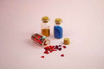 Red color, heart shape sequins spilled on the table from a tiny glass bottle. Glass bottles with craft glitter.