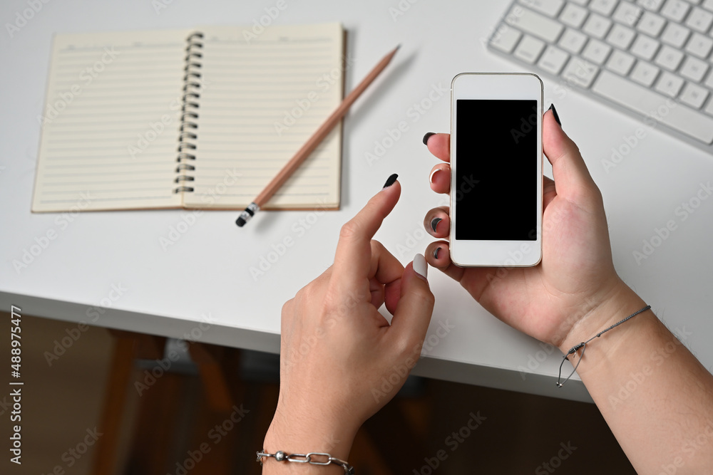 Poster top view of hands holding a smart phone with a black screen leaning on the white table with a note b
