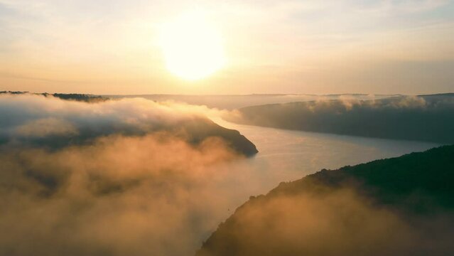 Side view of beautiful scenery of mist river valley at sunset. Panoramic view of picturesque valley with meandering foggy river flowing between hills with sunset on background. Concept of landscape
