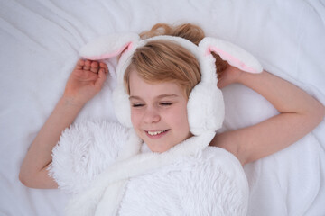 Beautiful little girl plays with rabbit ears. Easter concept. View from above. A child on a bed with a fluffy white blanket. Nice and cute picture