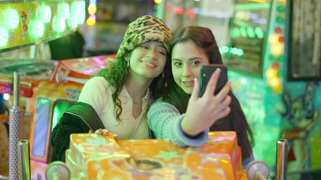 Valencia funfair - two friends take selfie pictures with smartphones sitting in roller coaster attraction car before departure at night
